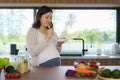 Beautiful Asian pregnant woman eating with lust cereals on breakfast in kitchen at home, enjoying meal. Yummy food for pregnant