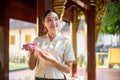 A beautiful Asian Thai woman in a traditional Thai-Lanna dress is in a temple, making a merit