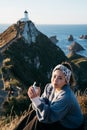 Beautiful asian tourist chilling out at Nugget Point, Dunedin, New Zealand. Young asian traveller enjoys coffee in morning at