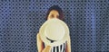 Beautiful Asian woman in black and white dress and holding white hat to close in half of her face with blue cotton background