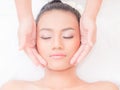 A beautiful Asian woman closes her eyes, relaxes in a spa shop with a facial massage from a professional masseuse Royalty Free Stock Photo