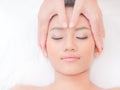 A beautiful Asian woman closes her eyes, relaxes in a spa shop with a facial massage from a professional masseuse Royalty Free Stock Photo