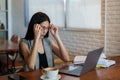 Beautiful asian woman coffee shop owner Hands on glasses, feeling a headache after concentrating on work on laptop computer. With