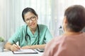 Beautiful Asian Woman Doctor in green uniform wear eyeglasses writing information in paper and talking giving advice to Senior Royalty Free Stock Photo