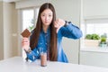 Beautiful Asian woman drinking chocolate milkshake and holding chocolate bar with angry face, negative sign showing dislike with Royalty Free Stock Photo