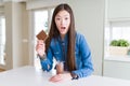 Beautiful Asian woman drinking chocolate milkshake and holding chocolate bar scared in shock with a surprise face, afraid and Royalty Free Stock Photo