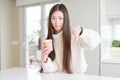 Beautiful Asian woman drinking a coffee in a take away paper cup with angry face, negative sign showing dislike with thumbs down, Royalty Free Stock Photo