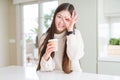 Beautiful Asian woman drinking a coffee in a take away paper cup with happy face smiling doing ok sign with hand on eye looking Royalty Free Stock Photo