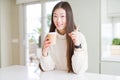 Beautiful Asian woman drinking a coffee in a take away paper cup surprised with an idea or question pointing finger with happy
