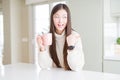 Beautiful Asian woman drinking a cup of coffee pointing and showing with thumb up to the side with happy face smiling Royalty Free Stock Photo