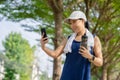 Beautiful Asian woman drinking water after jogging in the park. She is taking a picture of a water bottle with her smartphone Royalty Free Stock Photo