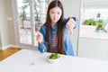 Beautiful Asian woman eating green fresh broccoli with angry face, negative sign showing dislike with thumbs down, rejection Royalty Free Stock Photo