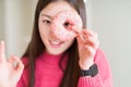 Beautiful Asian woman eating pink sugar donut doing ok sign with fingers, excellent symbol Royalty Free Stock Photo