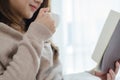 Beautiful asian woman enjoying warm coffee and reading book on bed in her bedroom. Royalty Free Stock Photo