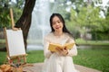 A beautiful Asian woman enjoys reading a book while picnicking in a green park on the weekend alone