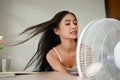 A beautiful Asian woman, feeling overheated, cools herself down with an electric fan
