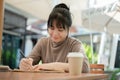 Beautiful Asian woman is focusing on writing some ideas in a book while sitting at an outdoors table Royalty Free Stock Photo