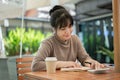 Beautiful Asian woman is focusing on writing some ideas in a book while sitting at an outdoors table Royalty Free Stock Photo