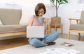 Beautiful Asian woman freelancer wear glasses sitting on the floor with laptop computer working while having mug of morning coffee Royalty Free Stock Photo