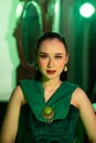 a beautiful Asian woman in a green dress has a very exotic face with ear and body jewelry while