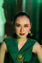 a beautiful Asian woman in a green dress has a very exotic face with ear and body jewelry while