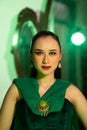 a beautiful Asian woman in a green dress has a very exotic face with ear and body jewelry while