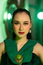 a beautiful Asian woman in a green dress has a very exotic face with ear and body jewelry while