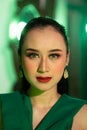 a beautiful Asian woman in a green dress has a very exotic face with ear and body jewelry while