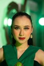 a beautiful Asian woman in a green dress has a very exotic face with ear and body jewelry while