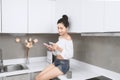 Beautiful Asian woman holding credit card and smartphone while sitting in kitchen Royalty Free Stock Photo