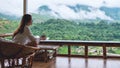 A beautiful asian woman holding and drinking hot coffee , sitting on balcony and looking at mountains and green