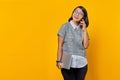 Beautiful asian woman holding laptop and talking on mobile phone over yellow background