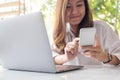 A beautiful Asian woman holding and looking at smart phone while using laptop in cafe Royalty Free Stock Photo