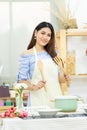 Beautiful Asian woman holding wooden cutlery behind dining table with pot , dish and kitchenware in the kitchen room with smiley