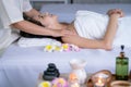 Beautiful Asian woman lie on bed and relax with spa massage from masseuse treat on her shoulder with other aroma accessories in Royalty Free Stock Photo