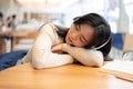A beautiful Asian woman is listening to music on her headphones and falling asleep on a table Royalty Free Stock Photo