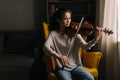 Beautiful asian woman musician playing the violin, sitting on soft chair. Royalty Free Stock Photo