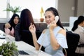 Beautiful Asian woman officer talking with customer by using landline phone at working desk in office with blurred background of Royalty Free Stock Photo