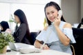 Beautiful Asian woman officer talking with customer by using landline phone at working desk in office with blurred background of Royalty Free Stock Photo