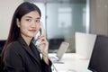 Beautiful Asian woman operator officer talking with customer by using landline phone at working desk in office with busy working Royalty Free Stock Photo