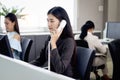 Beautiful Asian woman operator officer talking with customer by using landline phone at working desk in office with busy working Royalty Free Stock Photo