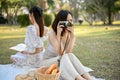 Beautiful Asian woman picnic with her friend in the park, taking a picture with her retro camera