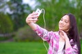 Beautiful asian woman in pink shirt smiling and making selfie in green summer park