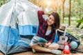 Beautiful Asian woman playing Ukulele in front of camping tent in pine woods. People and Lifestyles concept. Adventure and Travel