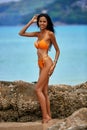 Beautiful asian girl in a orange bikini posing on a beach with rocks Royalty Free Stock Photo