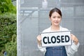 Beautiful Asian woman present banner with word closed in front of green house and sad emotion relate with close the business of