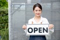 Beautiful Asian woman present banner with word open in front of green house and happy emotion relate with re-open the business