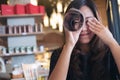 Asian woman roll a book and looking through it with one eye while closing another eye with feeling happy , sitting in cafe