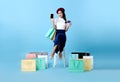 Beautiful Asian woman shopper sitting and carrying shopping bags with showing mobile phone and credit card in hands on blue