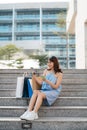 Beautiful Asian woman with shopping bags sitting on stairs while looking at smart phone and holding credit card Royalty Free Stock Photo